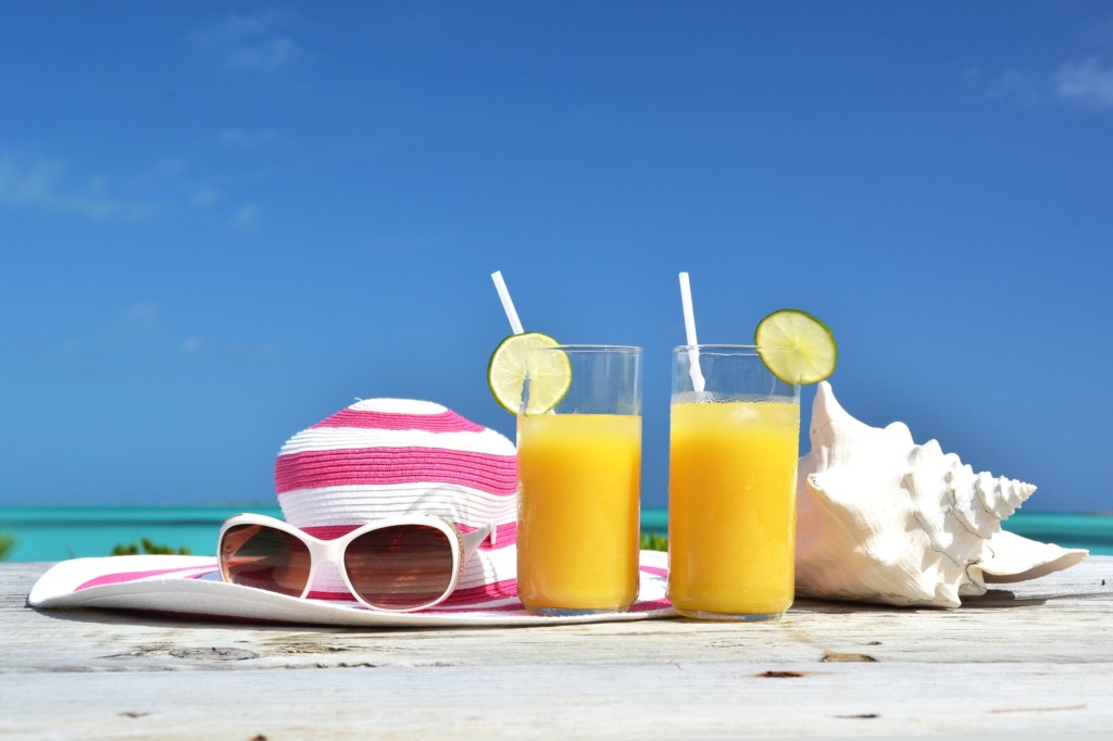 Jus d'orange, chapeau et lunettes de soleil sur une plage tropicale