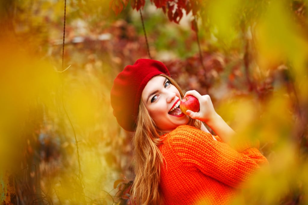 Jolie femme souriante avec un béret qui mange une pomme en automne